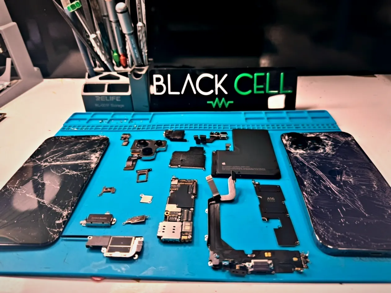 iPhone desarmado en el mesón de Blackcell: pantallas agrietadas, placa lógica y repuestos sobre la alfombra azul