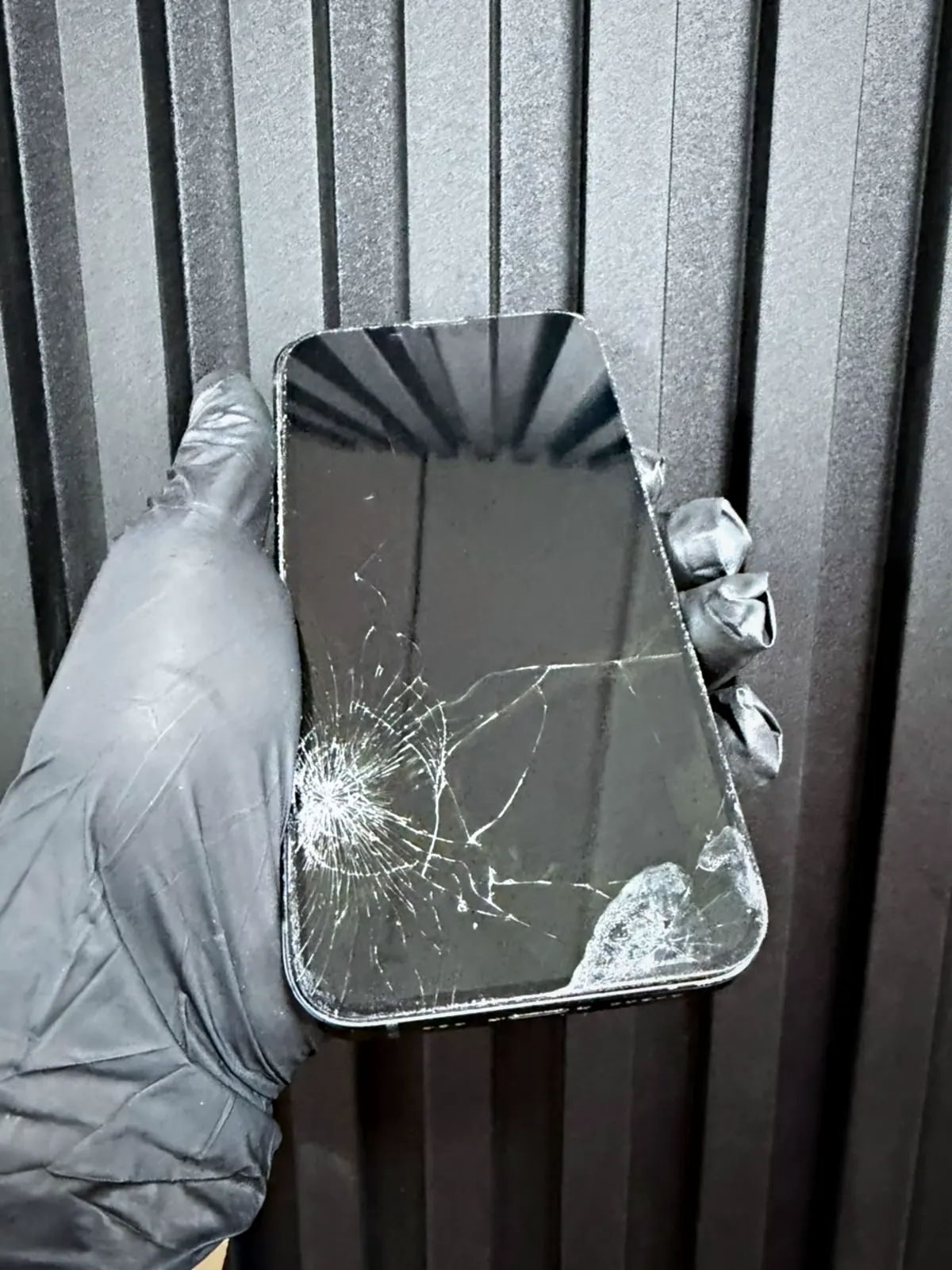 Pantalla de iPhone trizada sostenida con guante en el laboratorio